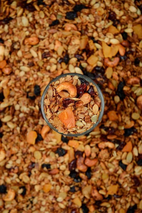 A glass of Wefeasto granola set in a bed of oats, nuts, seeds and dried fruit